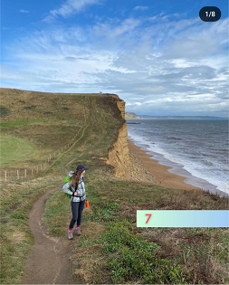 A white female with long brown hair looks out to sea while standing on the coastal path. 